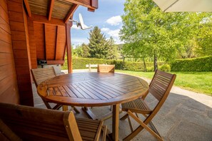 A wooden outdoor dining area with a round table and four chairs, a satellite dish, and a view of a well-maintained garden and trees. - New stylish chalet made in wood in the mountain (Xonrupt-Longemer)