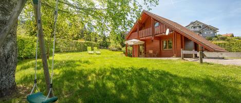 A wooden house with a balcony, a swing, and a well-maintained lawn.