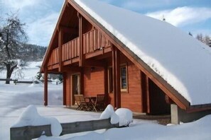 A wooden cabin with a sloped roof covered in snow, a porch with chairs, and a view of a snowy landscape. - New stylish chalet made in wood in the mountain (Xonrupt-Longemer)
