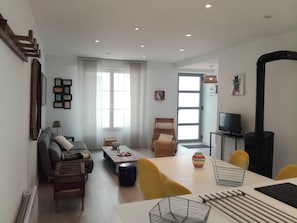 A modern living room with a sofa, coffee table, and chairs. There is a television, a fireplace, and a window with curtains.