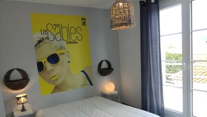 A bedroom with a large poster, a bed, a hanging light, and a window with curtains. - House with courtyard, 200 m from the Remblai and 3 minutes from Les Sables town center on foot! (Les Sables-D'olonne)