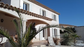A two-story building with a tiled roof, an arched entrance, and a patio area with outdoor furniture and plants. - Beautiful Villa (Bastide) close to the sea and Pic Saint Loup (Sussargues)