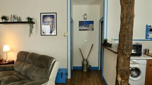 Una sala de estar con sofá, lámpara, un cuadro y una lavadora al fondo.