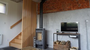Ein modernes Wohnzimmer mit Kaminofen, Fernseher auf einem Schrank und einer Treppe.