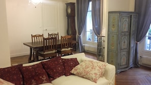 A living room with a sofa, a dining table with chairs, a clock, and a cabinet.
