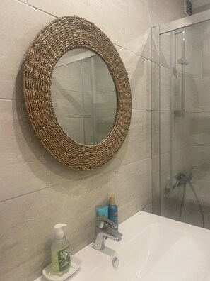 A bathroom with a round mirror, a sink, a handheld showerhead, and a bottle of hand soap.