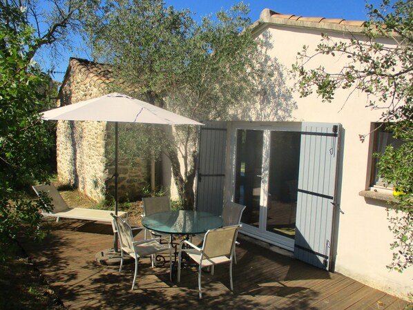 An outdoor patio with a glass table and chairs, a white umbrella, and a stone wall in the background. - In Uzès, 93m² airco+private terrace, sw.-pool 9X9, WIFI, huge garden, very quiet (Uzès)
