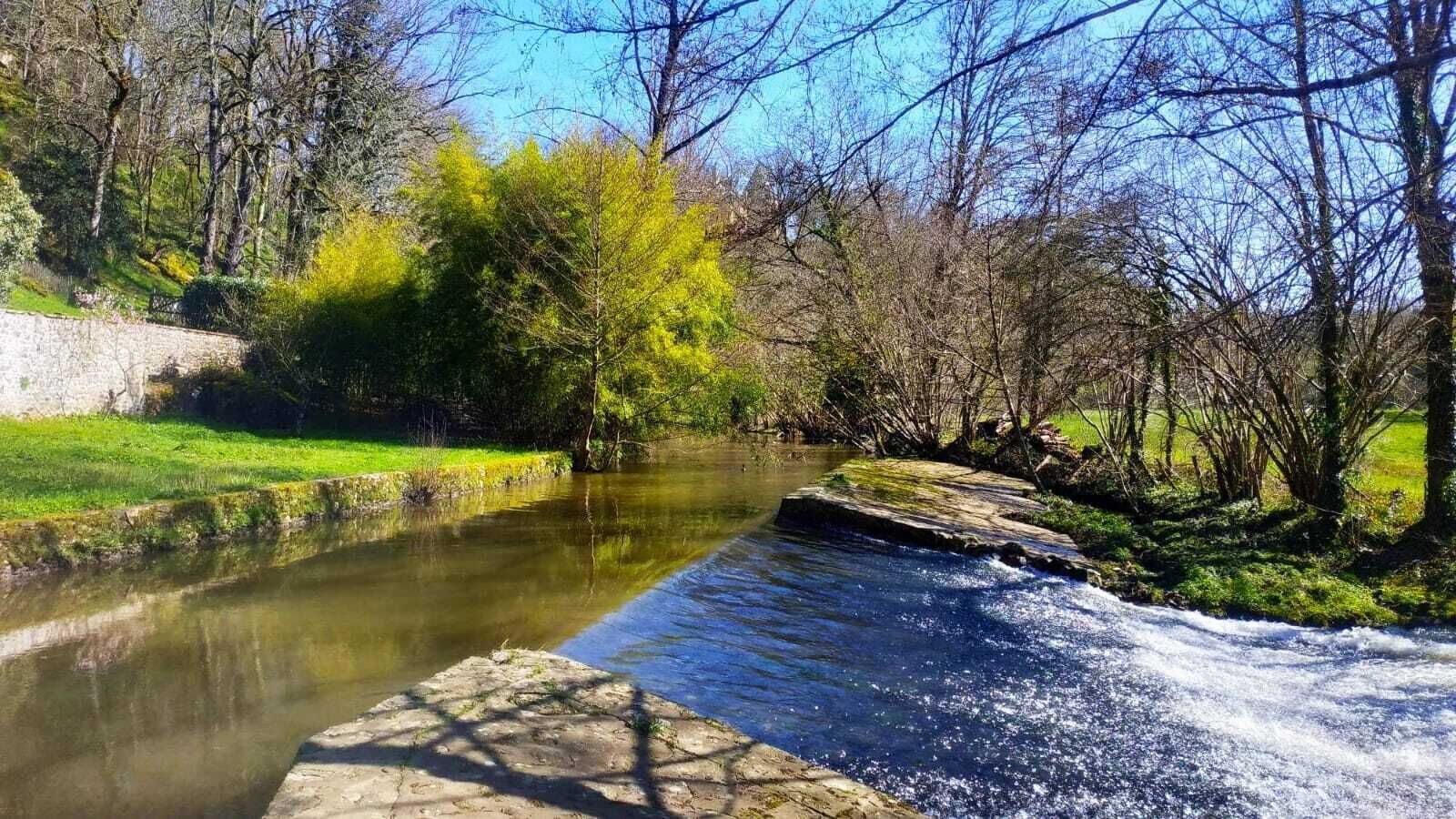 Une rivière qui traverse un parc bordé de murs de pierre et d’arbres.