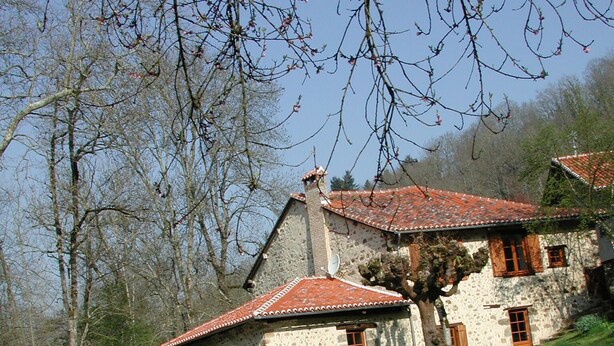 Un bâtiment rustique en pierre, surmonté d’un toit de tuiles rouges, qui se reflète dans une étendue d’eau calme.