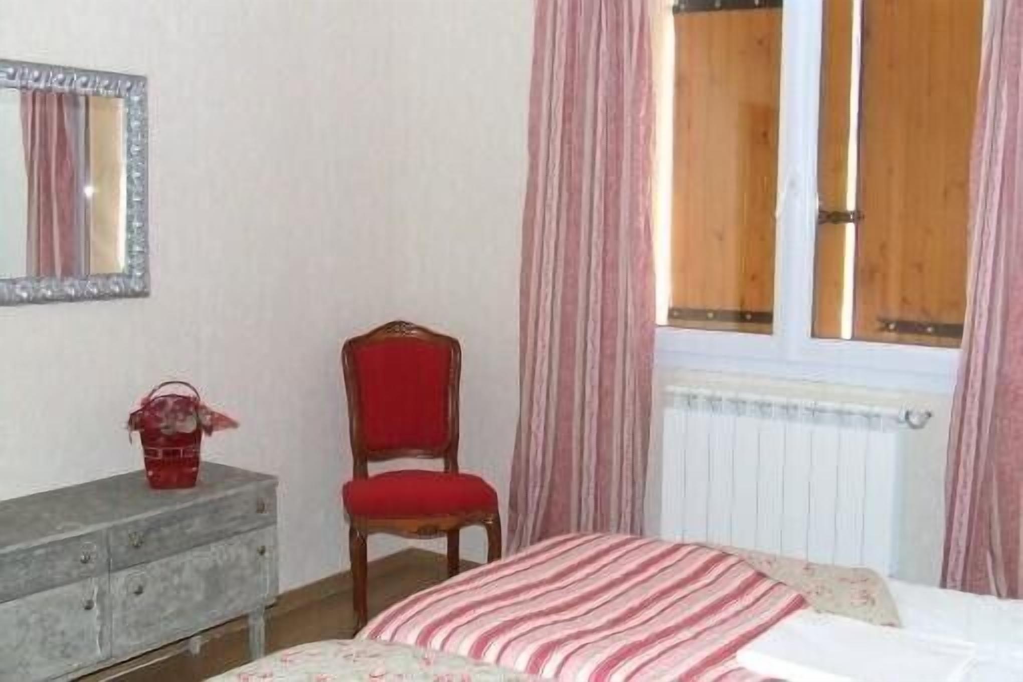 A bedroom with a bed, a dresser, a chair, a mirror, and a window with curtains.