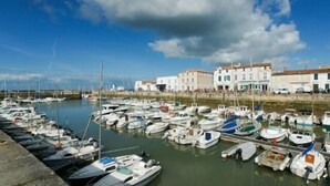 Ein Yachthafen mit zahlreichen vertäuten Booten, einer Uferpromenade und Gebäuden im mediterranen Baustil.