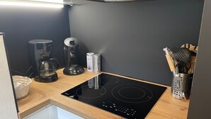 Eine Küche mit einer schwarzen Induktionskochplatte, einer Kaffeemaschine, einem Mixer und einem Küchenutensilien-Set.