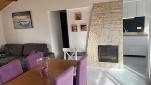 Ein modernes Wohnzimmer mit einem Holzespeisetisch, violetten Stühlen, einem Steinkamin und einer Küche im Hintergrund.
