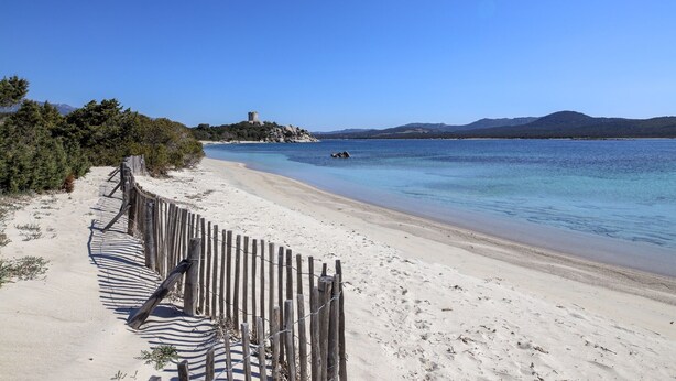 Una playa con una valla de madera y una torre en una pequeña isla al fondo.