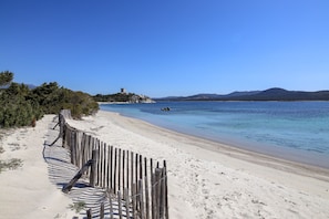 En strand med et træhegn og et tårn på en lille ø i baggrunden.