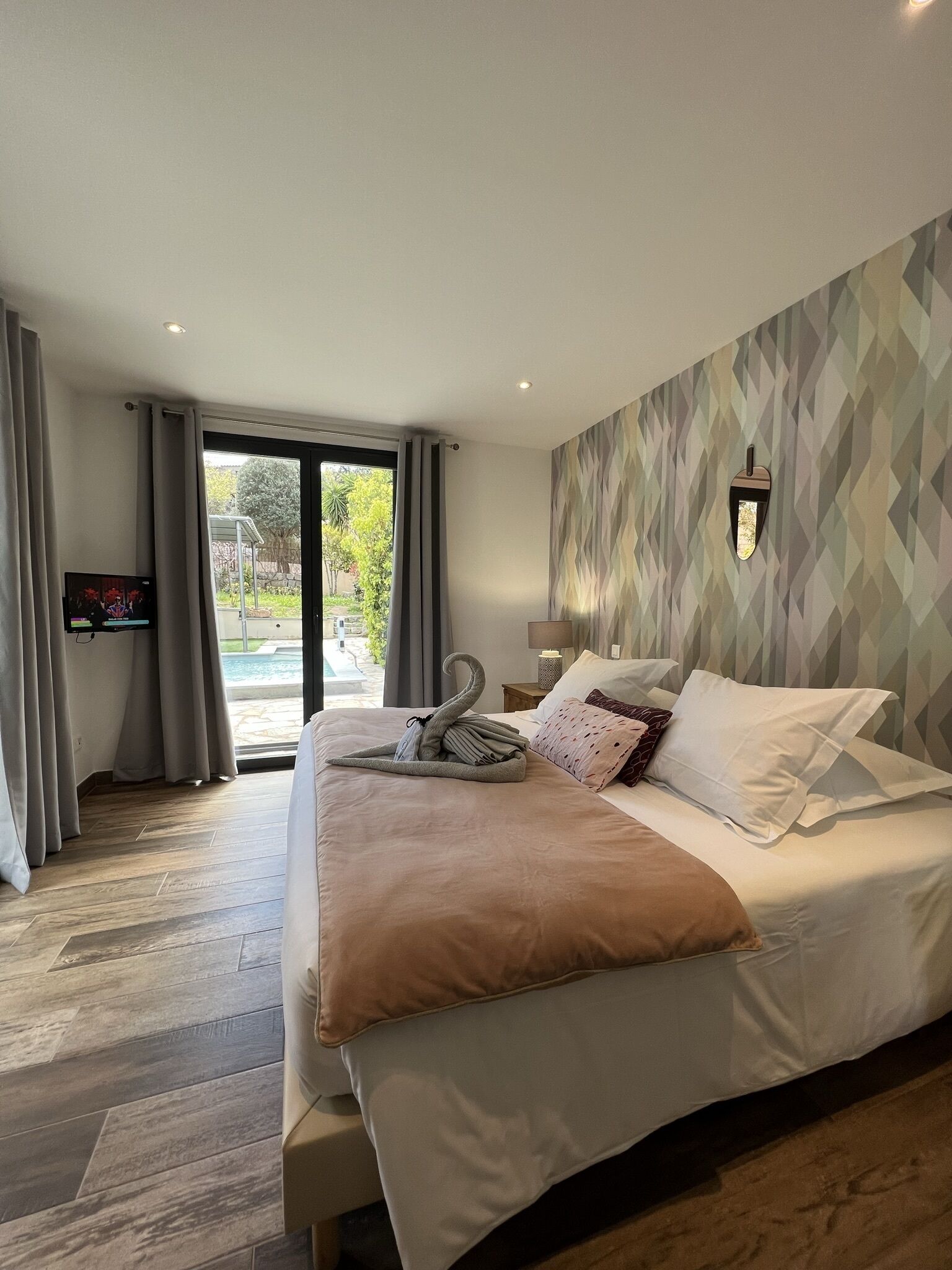 A modern hotel room with a large bed, a TV, and a view of a pool.