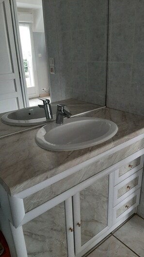 Un baño con lavamanos de mármol, un espejo y un mueble con cajones.