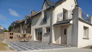 Ein zweigeschossiges Haus mit Balkon, einer Steinmauer und einer gepflasterten Terrasse mit Tisch und Stühlen.