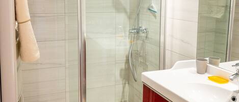 A modern bathroom with a glass-enclosed shower, a white sink with a red cabinet, and a mirror above the sink.