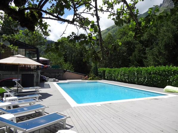 A swimming pool with lounge chairs and a covered area, surrounded by greenery and hills.