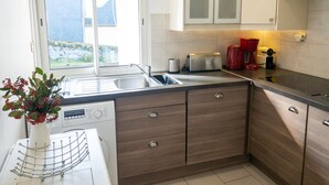 Una cocina moderna con lavavajillas integrado, tostadora, cafetera y ventana con vistas a una casa y jardín.