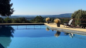 A clear blue pool with a view of distant hills, a fenced patio area with two lounge chairs and potted plants, and a metal railing. - GRANGE AUX AMIS in SARLAT, an ecolodge with a nice view  of the DORDOGNE valley (SARLAT)