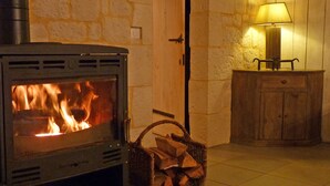 A wood-burning stove with logs, a basket of firewood, and a lamp on a wooden cabinet. - GRANGE AUX AMIS in SARLAT, an ecolodge with a nice view  of the DORDOGNE valley (SARLAT)