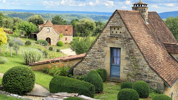 A stone cottage with a steeply pitched roof, surrounded by well-manicured hedges and a small garden. - GRANGE AUX AMIS in SARLAT, an ecolodge with a nice view  of the DORDOGNE valley (SARLAT)
