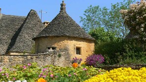 Un cottage in pietra con tetto di paglia, circondato da una varietà di fiori colorati.