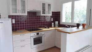 A compact kitchen with white cabinets, a built-in oven, a sink, and a window with a view of greenery outside. - Gîte La Salsepareille 6-person house near Pézenas with garden and air conditioning (Caux)