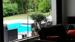 A living room with a large window overlooking a swimming pool and lush greenery. - beautiful modern villa with heated pool near: sea, golf, tennis and shops (Anglet)