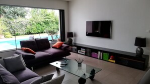 A modern living room with a sofa, coffee table, and a TV mounted on the wall. - beautiful modern villa with heated pool near: sea, golf, tennis and shops (Anglet)