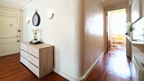 A hallway with a wooden floor, a white wall, a clock, and a small table with a vase of flowers. - Provencal Style and Large 1 Bedroom Rue Florian (Cannes)