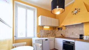 A compact kitchen with white cabinets, a built-in oven, and a dining area with a table and chairs. - Provencal Style and Large 1 Bedroom Rue Florian (Cannes)