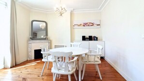 A dining area with a round table and white chairs, a chandelier, a fireplace, and a kitchen area with cabinets and a countertop. - Provencal Style and Large 1 Bedroom Rue Florian (Cannes)