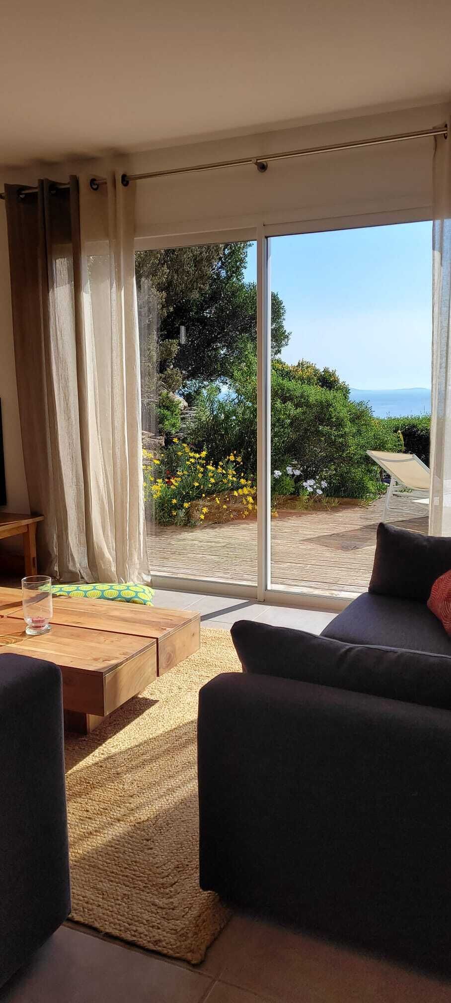Ein Wohnzimmer mit einer Couch, einem Couchtisch und Blick auf einen Garten durch große Glasfenster.
