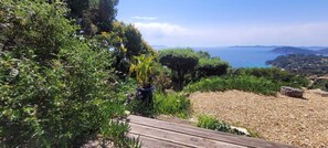 A coastal landscape with a wooden deck, dense greenery, and a view of the sea. - Sumptuous villa, comfortable, close to all amenities and beaches (Rayol-Canadel-Sur-Mer)