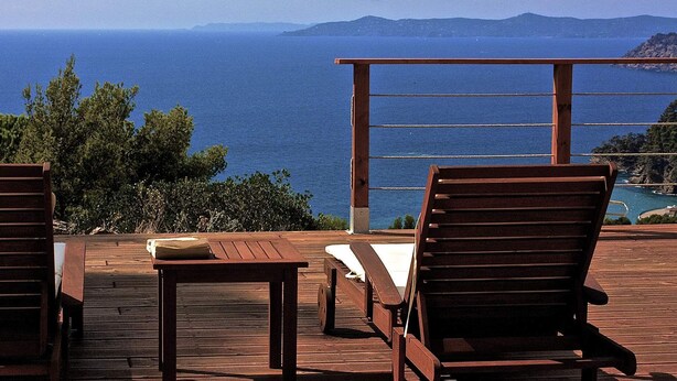 A wooden deck with two lounge chairs and a table, overlooking a coastal view with mountains in the distance. - Sumptuous villa, comfortable, close to all amenities and beaches (Rayol-Canadel-Sur-Mer)