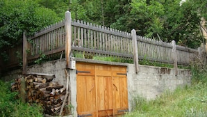 A rustic wooden gate with a concrete wall and a pile of logs.