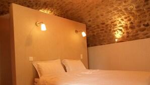 A bedroom with a stone ceiling, a bed with white bedding, and two wall-mounted lights. - HOUSE RENTAL IN CASTELJAU (Berrias-et-Casteljau)