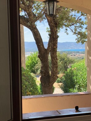 A window view of a tree-lined outdoor area with a clear sky and distant mountains.
