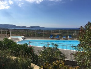 A pool with blue water, surrounded by a fence, and overlooking a scenic view of the sea and mountains.