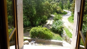 Blick durch ein Fenster auf einen Garten mit einer Steinmauer, einem Grill und einem Weg.