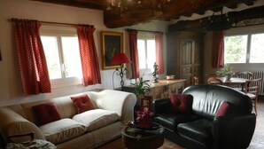 Una sala de estar acogedora con un sofá color beige, un sofá de cuero negro y una mesa de centro de madera. En el fondo, se distingue un comedor con una mesa y sillas.