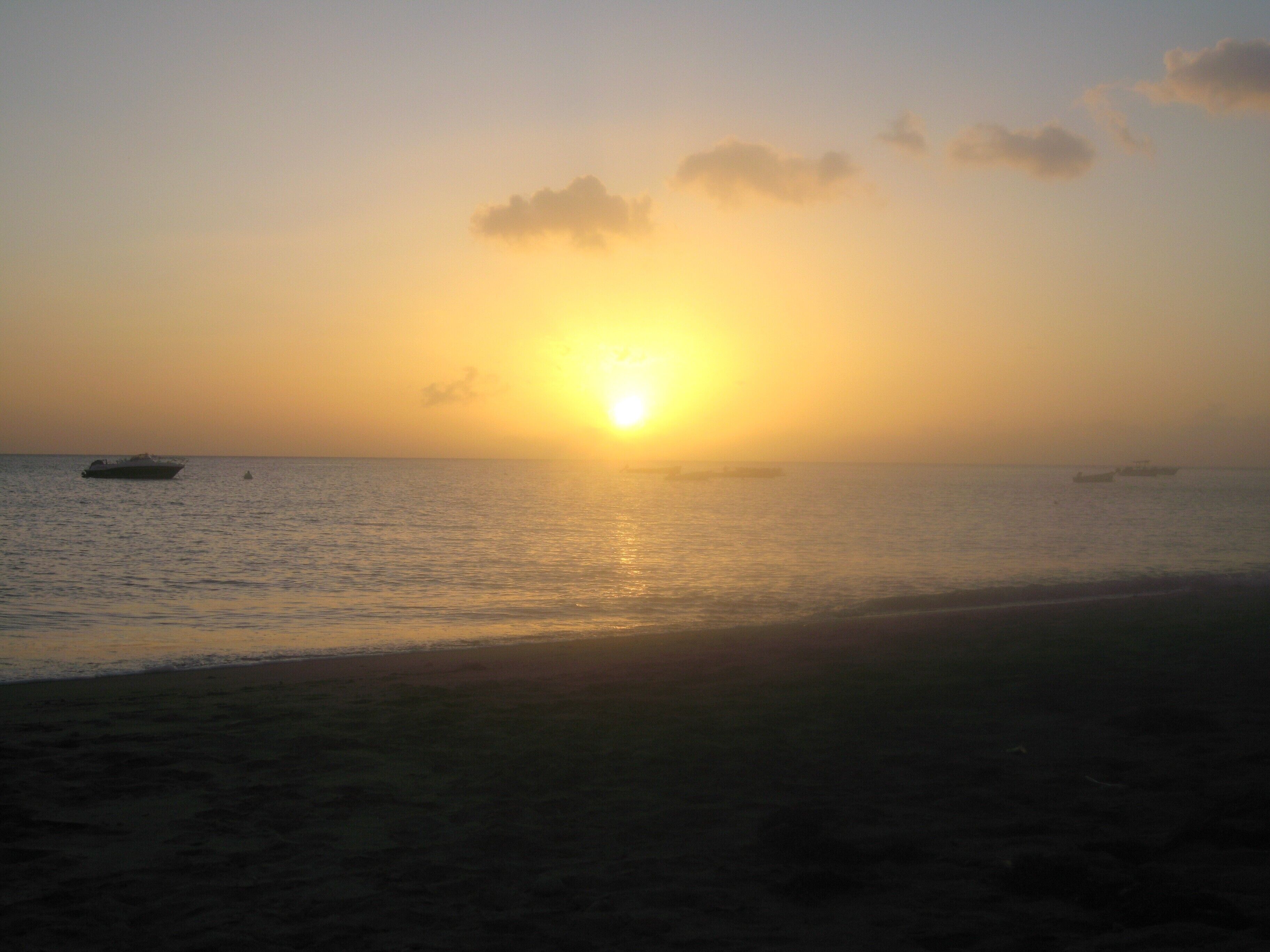Une plage au coucher du soleil, avec des bateaux sur l’eau.