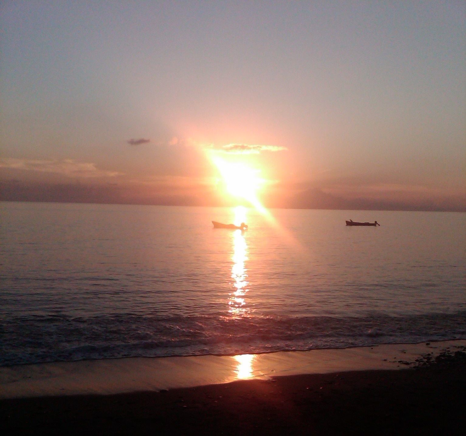 Un coucher de soleil sur une mer calme, avec un bateau à l’horizon.