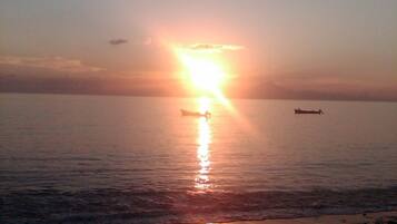 Un coucher de soleil sur une mer calme, avec un bateau à l’horizon.