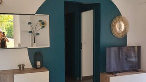 Moderni hotellihuone, jossa on turkoosinsävyinen holvikaari, joka johtaa käytävään. Huoneessa on suuri peili, litteänäyttöinen televisio ja kuviollinen päiväpeiteellä varustettu sänky.