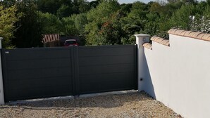A gated entrance with a closed black gate, a white wall with a tiled roof, and a signboard. - Comfortable, quiet "CôtéPlage" gîte-Covered terrace-Garden  (Vaux-Sur-Mer)
