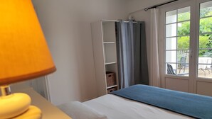 A bedroom with a bed, a window with curtains, a white wardrobe, and a lamp. - Comfortable, quiet "CôtéPlage" gîte-Covered terrace-Garden  (Vaux-Sur-Mer)